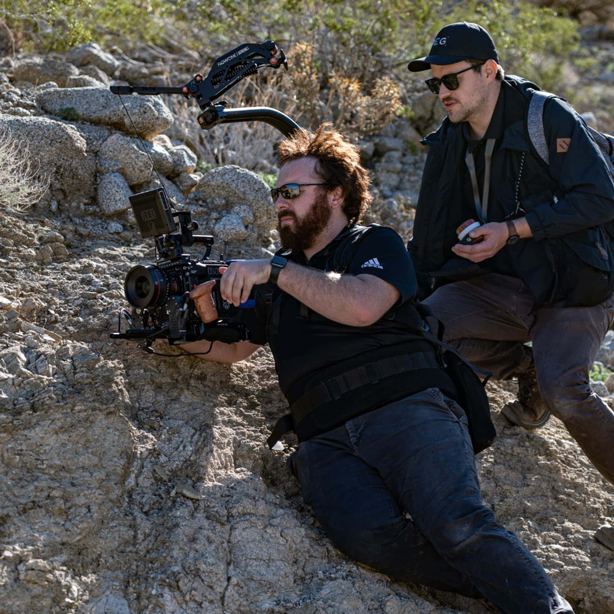 Two person camera crew perched on side of rock formation with RED V-Raptor XL round shape