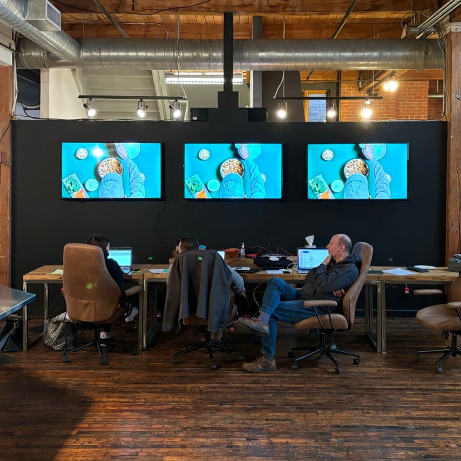 Three people sitting in chair in front of three monitors watching commercial filming round shape